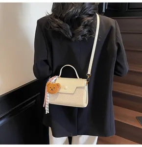 Close-up detail view of elegant women beige texture cross-body small square bag with cute bear.