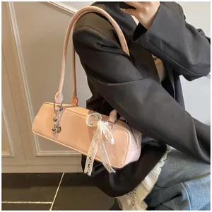 Pink patent leather baguette shoulder bag detail featuring a delicate white lace bow.
