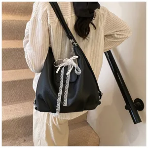 Detail view of the black leather backpack featuring elegant white lace pearl bow accessory.