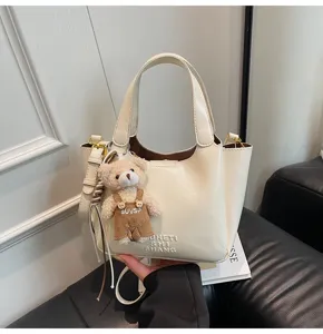 Elegante cremefarbene Leder-Tragetasche mit süßem Bärenanhänger, stilvolle Beuteltasche.