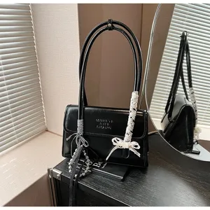 Detail shot of chic black shoulder handbag featuring double handles, lace bow and pearl charm.