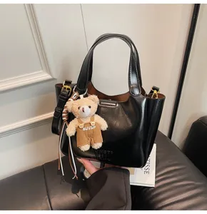 Klassische schwarze Leder-Eimer Tasche mit Henkeln und süßem kleinen Teddybär-Anhänger.