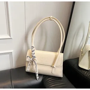 Detail shot of cream patent leather shoulder bag featuring chic ribbon bow and embossed lettering.