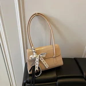 Chic French niche women shoulder bag, trendy patent leather handbag with ribbon and pearl pendant.