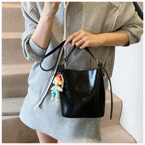 Chic black patent leather bucket bag with cute doll charm, stylish casual shoulder bag.