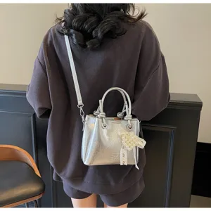 Stylish silver metallic bucket bag with top handle and chic pearl bow pendant for women.