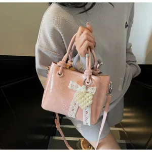 Detail shot of pink patent leather bucket bag featuring sweet bow and elegant pearl charm design.