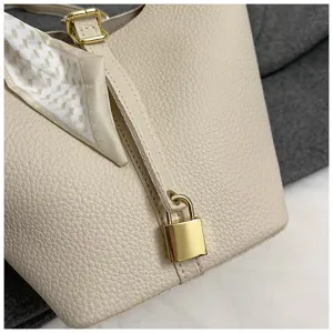 Nahaufnahme der beige ledernen Eimer Tasche mit goldenem Vorhängeschloss und Seidentuch.