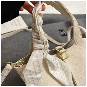 Nahaufnahme des beige Leder Eimer Tasche Griffs verziert mit stilvollem Seidenschal.