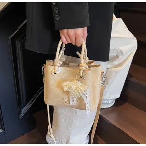 Close-up detail of a chic beige bucket handbag featuring pearl lace pendant and shoulder strap.
