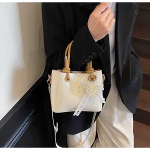 Close-up detail shot of the chic white patent bucket bag featuring pearl heart pendant and tan handles.