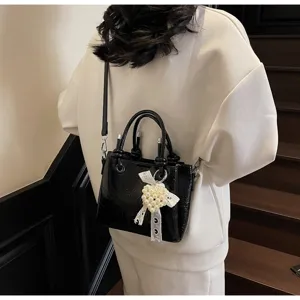Detailed view of a stylish black patent leather shoulder bag with a pearl bow charm.