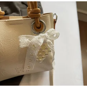 Cream textured bucket bag featuring a knotted handle and lace pearl bow pendant detail