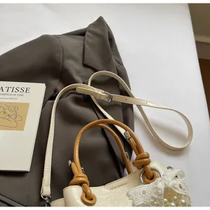 Detail view of stylish bucket bag with brown knotted handle and delicate lace pearl bow accent.