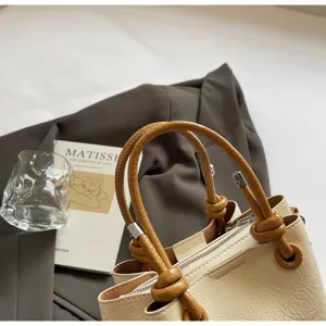 Detail view of stylish beige bucket bag with brown knotted handles, elegant lifestyle prop setup.