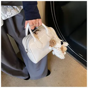 Detail shot of a stylish white patent leather bowling bag featuring a cute plush pendant.