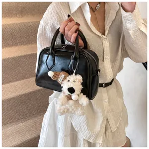 Black soft leather bowling bag for women, trendy top handle pillow bag with cute plush keychain.