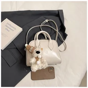 Close-up detail of cream soft leather bowling bag with cute bear charm and shoulder strap.