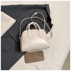Minimalist beige bowling bag detail shot featuring soft leather, top handles, and cross-body strap.
