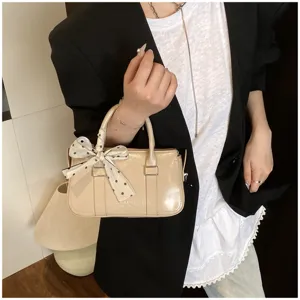 Detailed view of beige patent leather handbag with chic polka dot ribbon decoration.