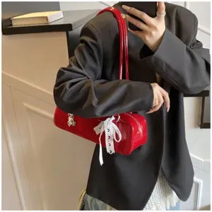 Red patent leather baguette shoulder bag detail featuring a cute white bow and metal pendant charm.