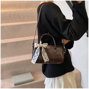 Detail view of a brown patent leather handbag featuring a chic polka dot ribbon bow and strap.