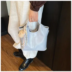 Nahaufnahme einer hellblauen Handtasche aus weichem Leder mit niedlichem Plüschbärchenanhänger.