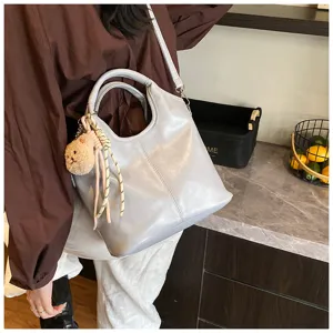 Weiche Leder-Umhängetasche Detail, stilvolle graue Tasche mit Bärenanhänger und lässigem Design.