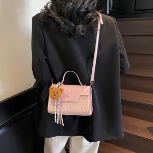 Pink PU leather crossbody shoulder bag for women with cute bear charm and top handle.