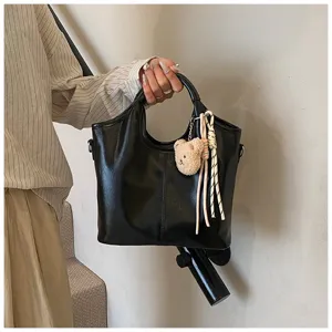 Schwarze weiche Ledertasche Detailansicht mit süßem Bärenanhänger und geflochtenem Seil.