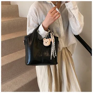 Detailansicht einer schwarzen weichen Ledertasche mit einem süßen Bären-Plüschanhänger.
