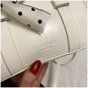Detail view of a trendy white women handbag featuring metal buckles and chic polka dot ribbon.