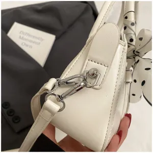 Detailed view of white PU leather women handbag with silver hardware and polka dot silk scarf.