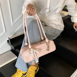 Pink patent leather baguette shoulder bag with chic lace bow and metal charm accessory.