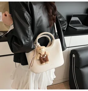 Nahaufnahme der eleganten weißen Handtasche mit geflochtenen Griffen und Bärenanhänger.