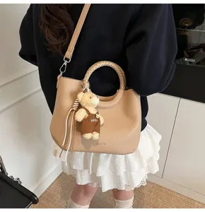 Detailaufnahme einer stilvollen beige Handtasche mit geflochtenem Rundgriff und Bärenanhänger.