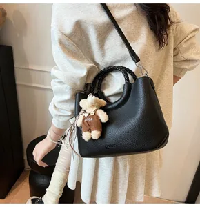 Schicke schwarze Handtasche aus geflochtenem Leder mit süßem Bärenanhänger für Damen.