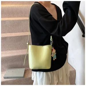 Detail shot of stylish light green bucket bag worn on model, showing shoulder strap and charm.