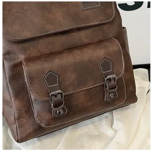 Détail du sac à dos rétro en similicuir marron souple, doté de coutures blanches contrastées.