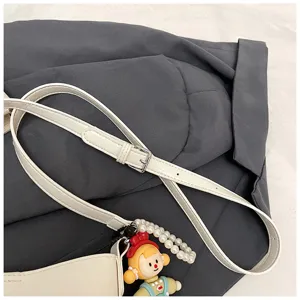 Detailed view of white shoulder bag strap with cute cartoon doll and pearl charm pendant.