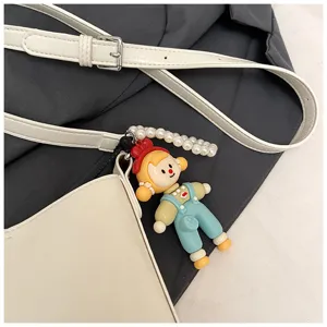 Close up detail of white shoulder bag featuring pearl strap and cute cartoon doll pendant.