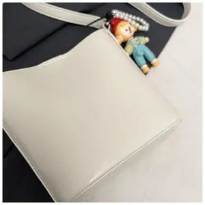 Close-up detail of white minimalist bucket shoulder bag with cute doll pendant and pearl chain.