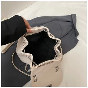 Vue détaillée du sac à dos seau matelassé en cuir crème avec chaîne argentée et cordon de serrage.