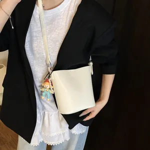 Minimalist white bucket bag for women, stylish PU leather shoulder crossbody bag with cute doll charm.