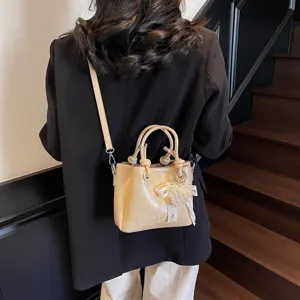 Stylish patent leather bucket bag with handle and pearl lace pendant, perfect for daily commuting.
