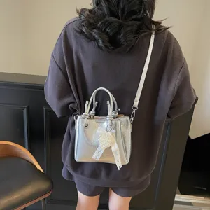 Stylish silver metallic bucket bag for women with pearl ribbon charm and shoulder strap.