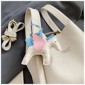Detail shot of beige bucket bag featuring a cute winged horse charm and detachable strap.