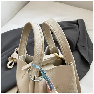 Detailed view of the chic cream-white leather bucket handbag, featuring top handles and hardware.