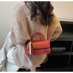 Detail shot of women's red leather shoulder bag with wooden bead charm and metal buckle accent.