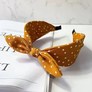 Close-up detail of a retro mustard yellow polka dot bow headband, soft fabric and stylish wide design.